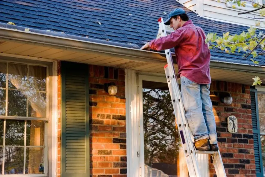 man cleaning gutters on a ladder