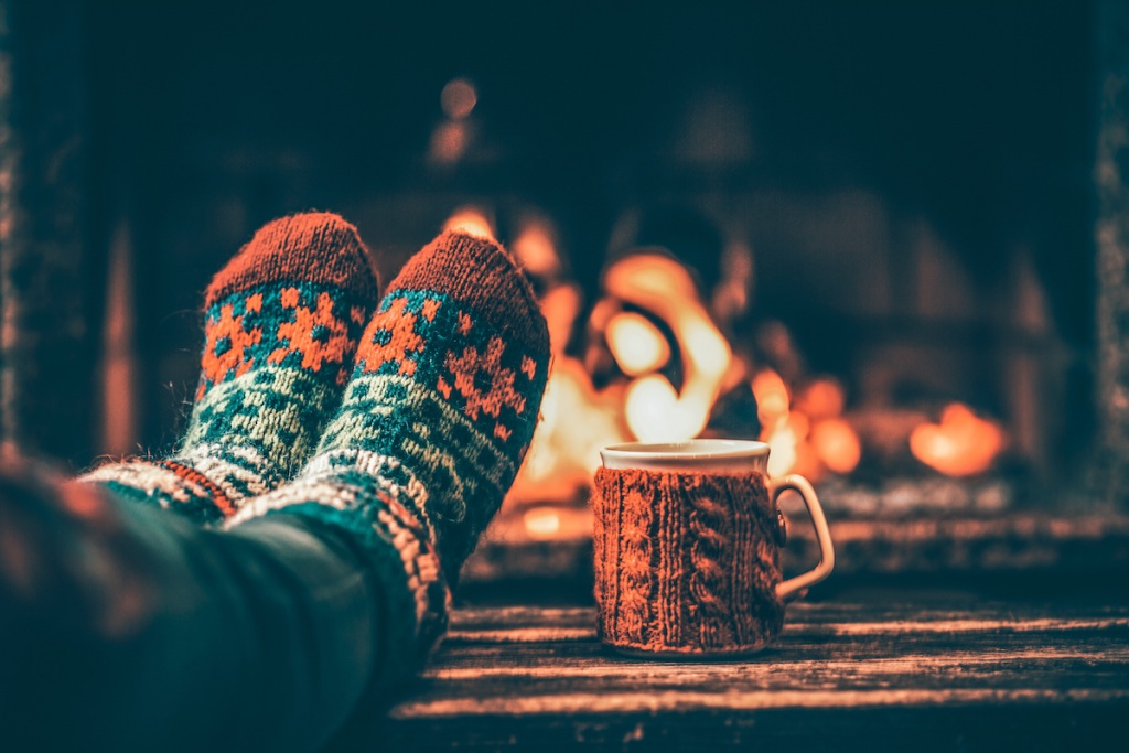 Burlington home buyers | Feet in woollen socks by the Christmas fireplace. Woman relaxes by warm fire with a cup of hot drink and warming up her feet in woollen socks. Close up on feet. Winter and Christmas holidays
